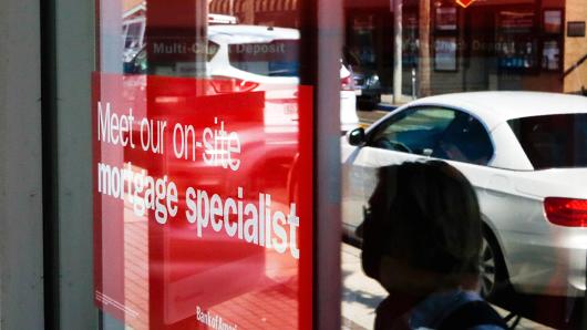 The reflection of pedestrians walking is seen in a window next to a sign advertising home mortgage services at a Bank of America Corp. branch in Manhattan Beach, California.