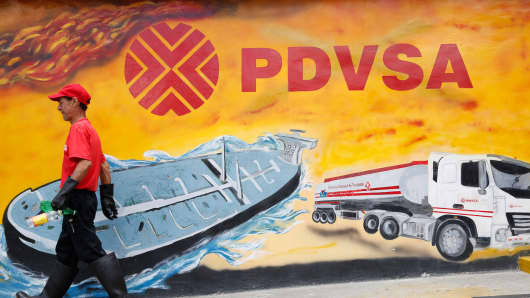 A worker walks past a mural with a PDVSA logo at its gas station in Caracas, Venezuela, August 29, 2014.