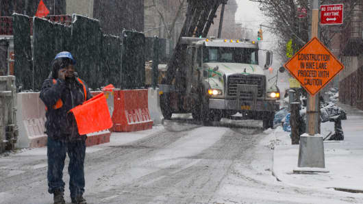 A worker talks on a mobile phone while it snows during construction of a residential building in New York.