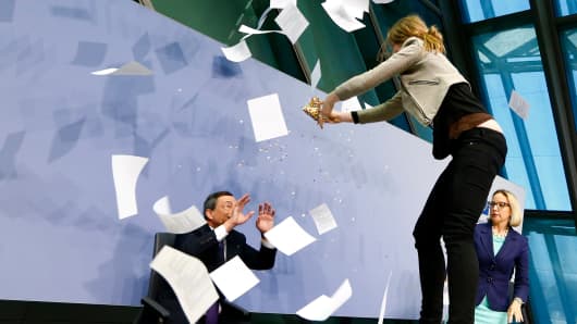 A protester jumps on the table in front of the European Central Bank President Mario Draghi during a news conference in Frankfurt, April 15, 2015.