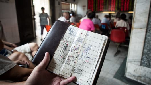 An investor holds a notebook showing stock market movements, as he sits at a brokerage house in Shanghai, China.