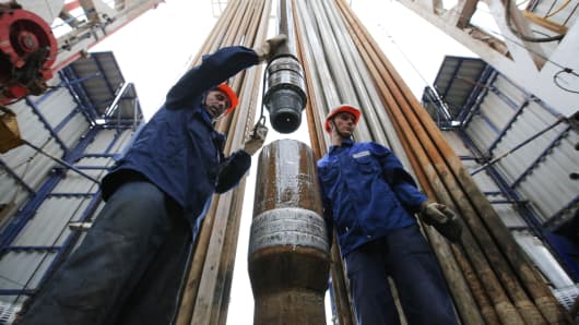 Workers secure drilling pipe sections on an oil drilling tower