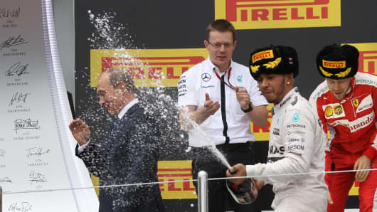 Russian President Vladimir Putin (L) attends the Formula 1 Russian Grand Prix competition as Lewis Hamilton (2nd R) of Great Britain and Mercedes GP and Sebastian Vettel (R) of Germany and Ferrari celebrate October 11, 2015 in Sochi, Russia.
