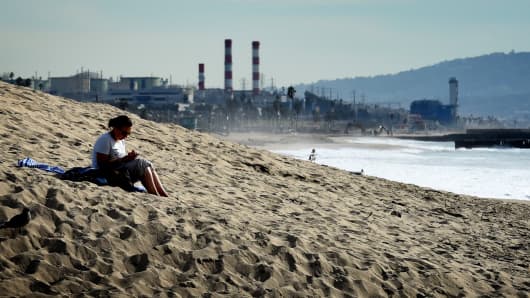 A woman sits on a sand berm created by city workers to protect houses from El Nino storms and high tides at Playa Del Rey beach in Los Angeles, on November 30, 2015.