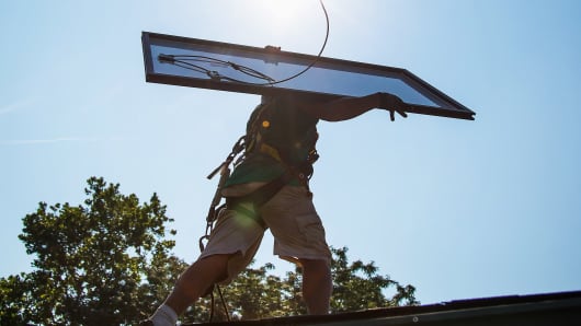 A SolarCity employee carries a solar panel on the roof during installation at a home in Kendall Park, N.J.
