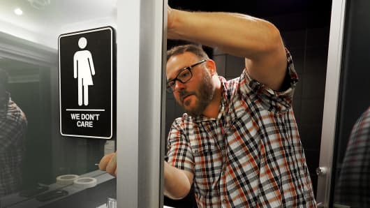 Museum manager Jeff Bell adheres informative backing to gender-neutral signs in the 21C Museum Hotel public restrooms on May 10, 2016, in Durham, North Carolina.