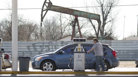 A motorist fills her car with gas at a gas station near an oil field pumping rig in Oklahoma City, Oklahoma.