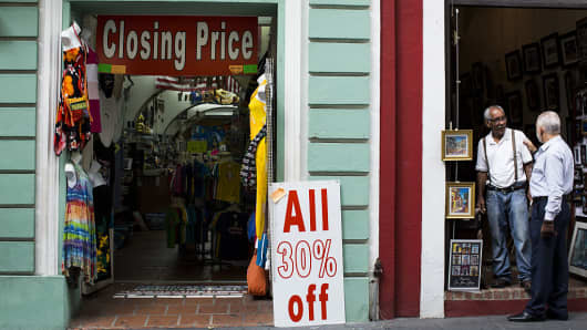 Two men speak outside a store displaying a 'Closing Price' sign in Old San Juan, Puerto Rico, on Friday, April 29, 2016.