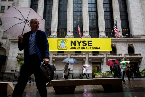 Pedestrians hold umbrellas while walking past a Snapchat sign displayed outside of the New York Stock Exchange.