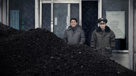 his picture taken on December 14, 2012 from China's northeastern city of Dandong, looking across the border, shows a North Korean military officer (R) and a North Korea man (L) standing behind a pile of coal along the banks of the Yalu River in the northeast of the North Korean border town of Siniuju.