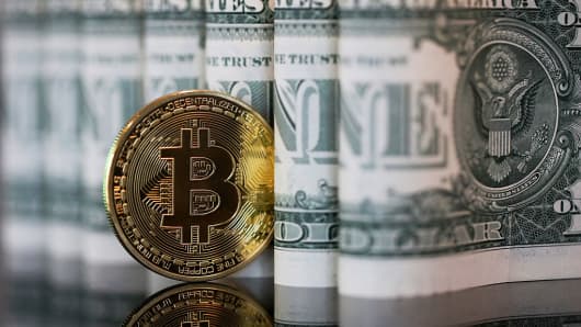Un token Bitcoin se encuentra junto a una colección de US billetes de un dólar en este dispuesto fotografía en Londres, Reino Unido, el miércoles 4 de enero, 2017.