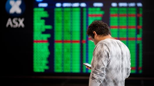 A man uses his mobile phone in front of electronic stock boards at the Australian Securities Exchange (ASX Ltd.) headquarters in Sydney, Australia.