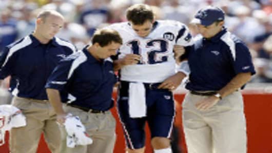 New England Patriots quarterback Tom Brady is helped off the field by medical personnel after being hit during play.