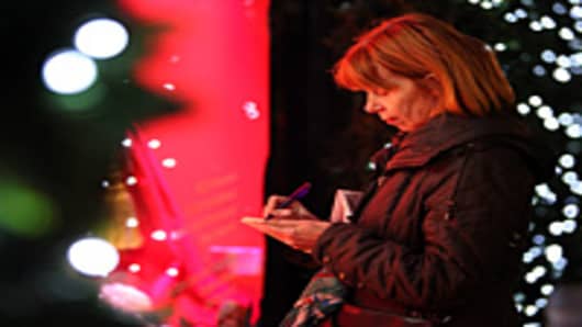 A woman makes a shopping list in front of a department store's Christmas window display.