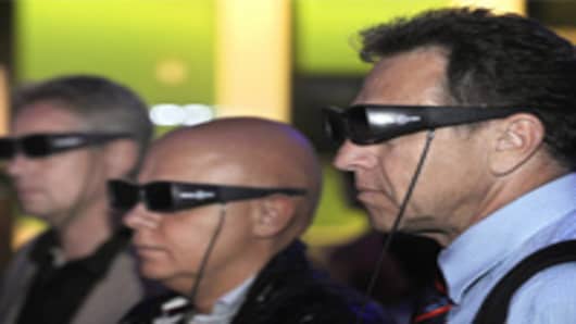 Fairgoers wear special '3D' glasses as they watch a movie on a 3D TV screen.