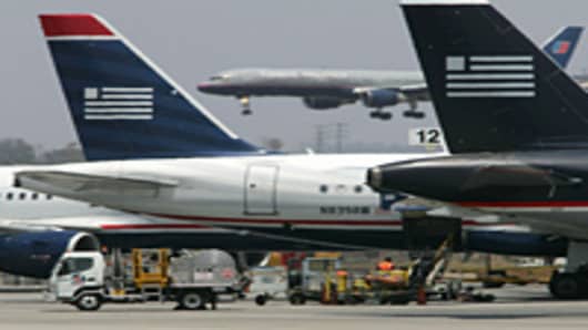 A United Airlines jet lands as US Airways jets are prepared for flight at Los Angles International Airport.