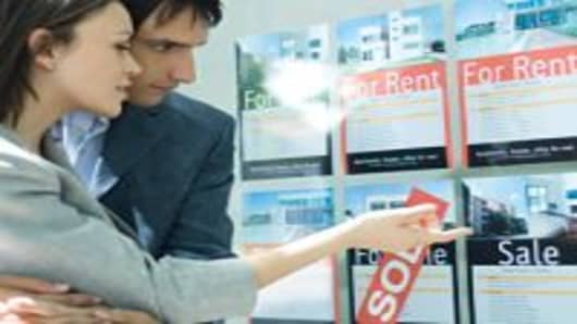 Couple looking at properties in window of real estate agency.