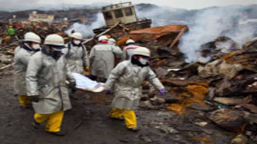 Rescue workers carry a body from the rubble of a village destroyed by the devastating earthquake, fires and tsunami March 16, 2011 in Kesennuma, Miyagi province, Japan.