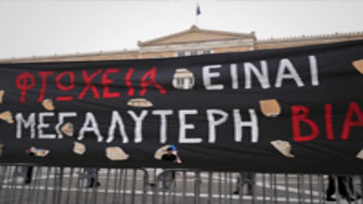 Greek riot police officers stand guard in front of the Greek parliament next to a banner reading ' Poverty is the biggest brutality ' during a general strike against government austerity plans, in Athens.