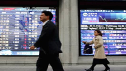 Investors pass by an electric board showing the figure of Nikkei stock average in Tokyo, Japan.