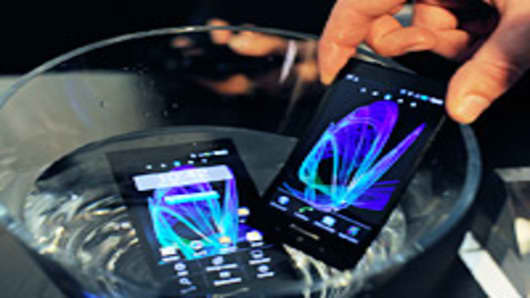 An employee uses a bowl of water to demonstrate the waterproof properties of Panasonic Corp. Eluga smartphones at the Mobile World Congress in Barcelona, Spain, on Tuesday, Feb. 28, 2012.