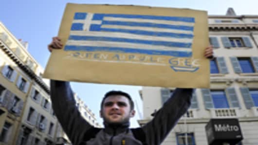 A man holds a placard bearing the Greek flag.