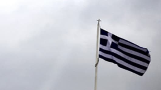 The Greek national flag is seen flying above the parliament building on Syntagma Square in Athens, Greece, on Thursday, Feb. 16, 2012.