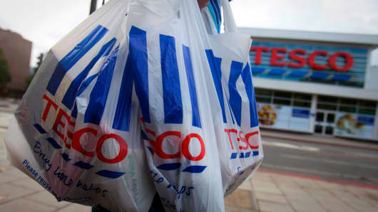 A customer carries Tesco-branded shopping bags as she leaves one of the company's stores.