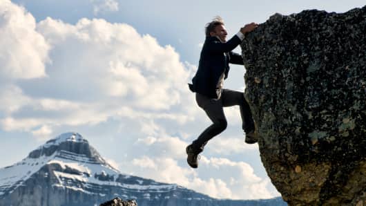 Businessman struggles to climb mountain summit.