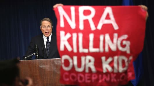 A demonstrator from CodePink holds up a banner as National Rifle Association Executive Vice President Wayne LaPierre delivers remarks during a news conference.