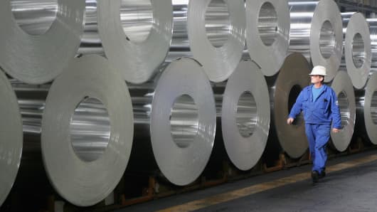 A worker walks among rolls of semi-finished aluminum at an Alcoa aluminum factory.