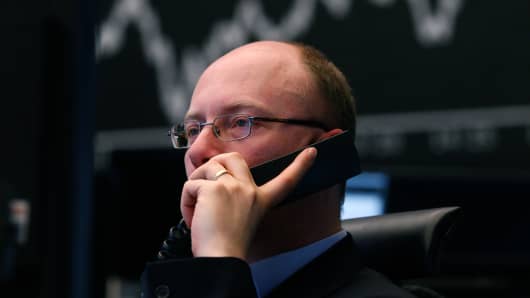 A financial trader uses a telephone as he monitors data on his computer screens in front of a display of the DAX Index curve at the Frankfurt Stock Exchange.