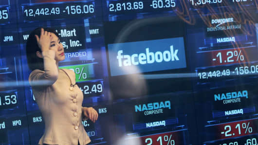 A television reporter is seen inside the Nasdaq studios as the Facebook logo is displayed on a ticker board.