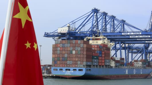 A Chinese flag flies on a vessel moving past shipping containers being unloaded at a Tianjin Port Group Co. dock in Tianjin, China.