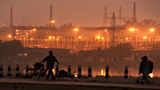 Pedestrians walk on a roadside past a power sub-station in the outskirts of Kolkata.