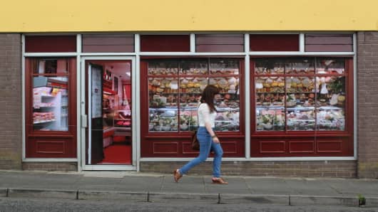 A pedestrian walks pass stickers applied to the windows of a former butcher’s shop in Belcoo, Northern Ireland, outside Enniskillen on June 1, 2013.