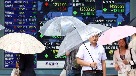 Pedestrians with umbrellas walk past an electronic stock board in Tokyo, Japan.