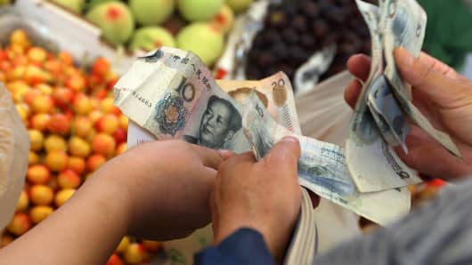 A shopper counts Chinese yuan banknotes as he shops for fruit and vegetables at a market in Shanghai, China.