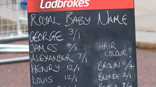 A woman holds a Ladbrokes board listing possible baby names to bet on as media gather outside Buckingham Palace to read the easel displaying the announcement of the son of The Duke and Duchess of Cambridge on July 23, 2013 in London, England.