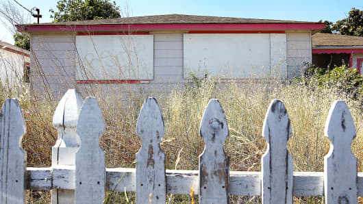 Weeds grow past the height of a picket fence in front of an abandoned house in Richmond, California.