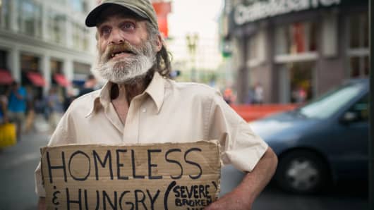 A homeless man holding a sign asking for a donation from bystander in San Francisco, California.