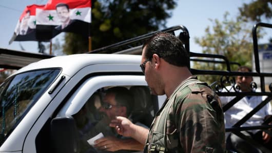 A Syrian military soldier checks a man's identification at a check point on Baghdad street, in Damascus, Syria, Wednesday, Aug. 21, 2013.