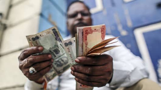 A man counts Indian rupee notes near the Bombay Stock Exchange building.