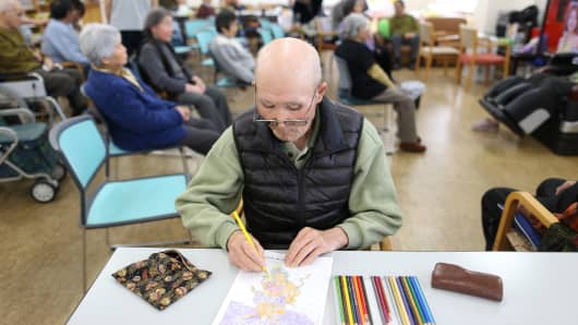 An elderly man does a coloring exercise at a day care facility, Japan.