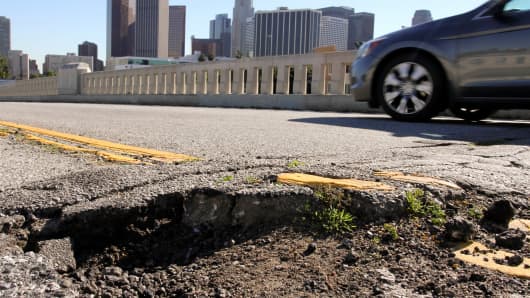 A car drives past potholes and broken asphalt on West 1st Street in Los Angeles, California.