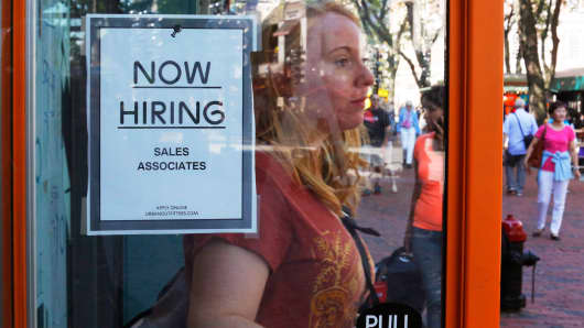 A woman walks past a "Now Hiring" sign as she leaves the Urban Outfitters store at Quincy Market in Boston.