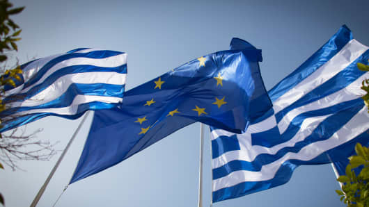 The national flag of Greece and the flag of the European Union fly above a government building in Athens.