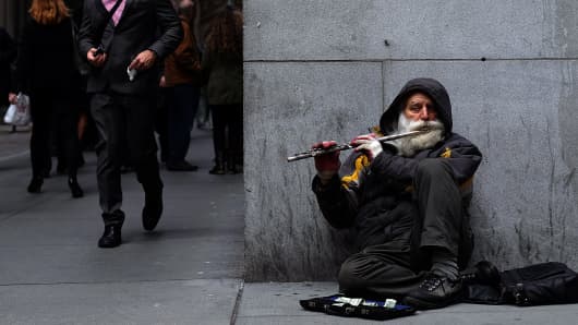 A musician plays a flute sitting on the footpath next to New York Stock Exchange (NYSE) building in New York.