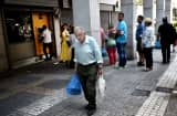An elderly man walks in front of a bank as people queue to withdraw cash from an ATM machine in central Athens on June 30, 2015.