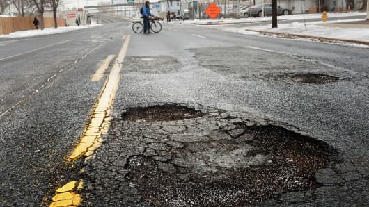 A man walks his bike across the street in front of a large pothole at Eighth Avenue and Kalamath Street in Denver.